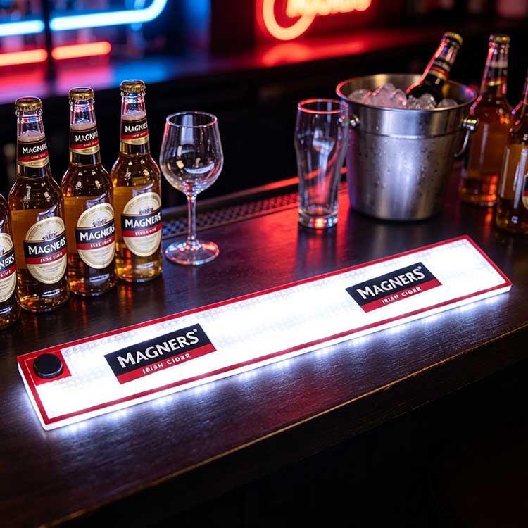 Full commercial serving station shot of battery operated LED bar runner on dark pub counter, lined with complete Magners cider bottle lineup, wine glasses, pint glasses and ice bucket for busy bar service