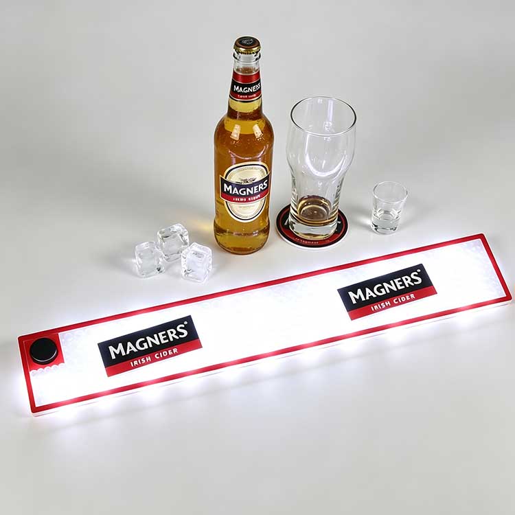 Commercial LED Bar Runner with Magners Irish Cider logo, battery operated glowing illuminated bar spill mat, waterproof non-slip drip channel surface laid on clean white counter with cider bottle, glasses and ice cubes