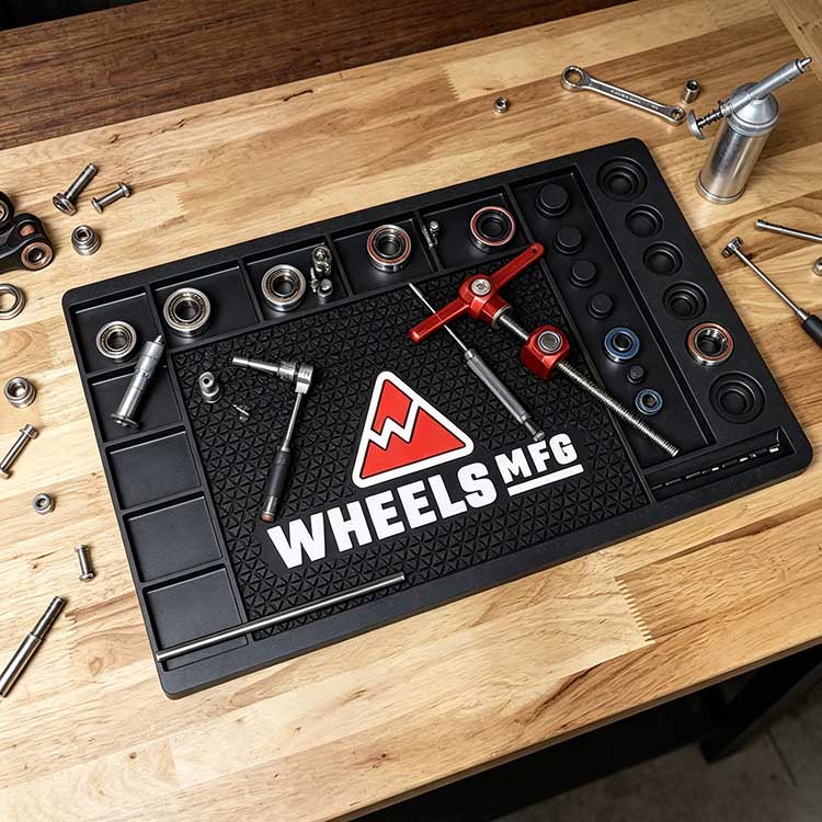 Heavy-duty rubber workbench mat in a wooden workshop setting, holding bike bearing press tools and components for professional repair