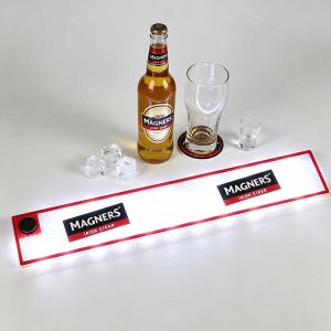 Commercial LED Bar Runner with Magners Irish Cider logo, battery operated glowing illuminated bar spill mat, waterproof non-slip drip channel surface laid on clean white counter with cider bottle, glasses and ice cubes
