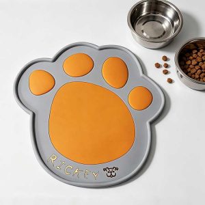 Grey silicone dog mat with a vibrant orange paw print and custom name.